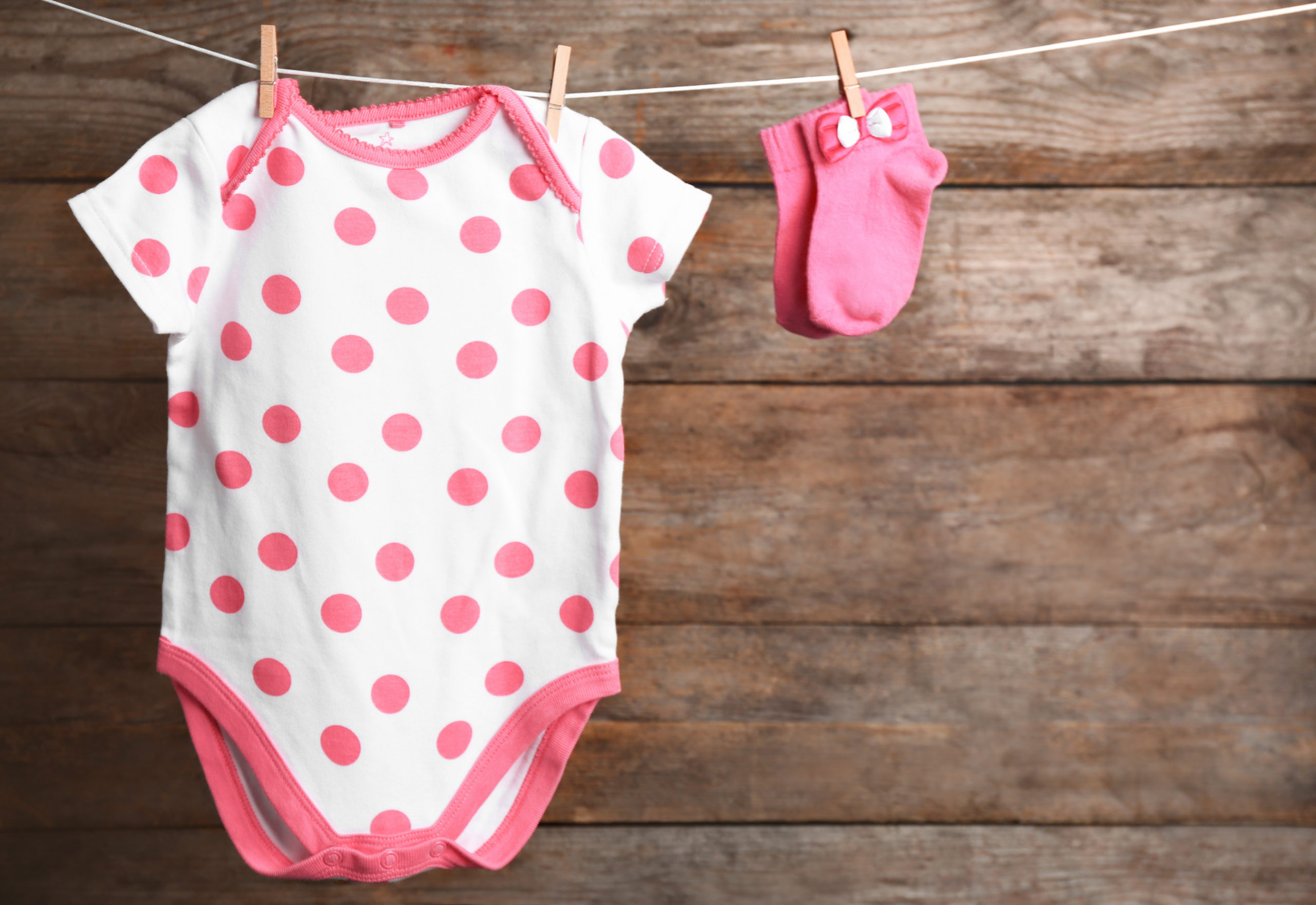 Bodysuit and socks on laundry line against wooden background, space for text. Baby accessories