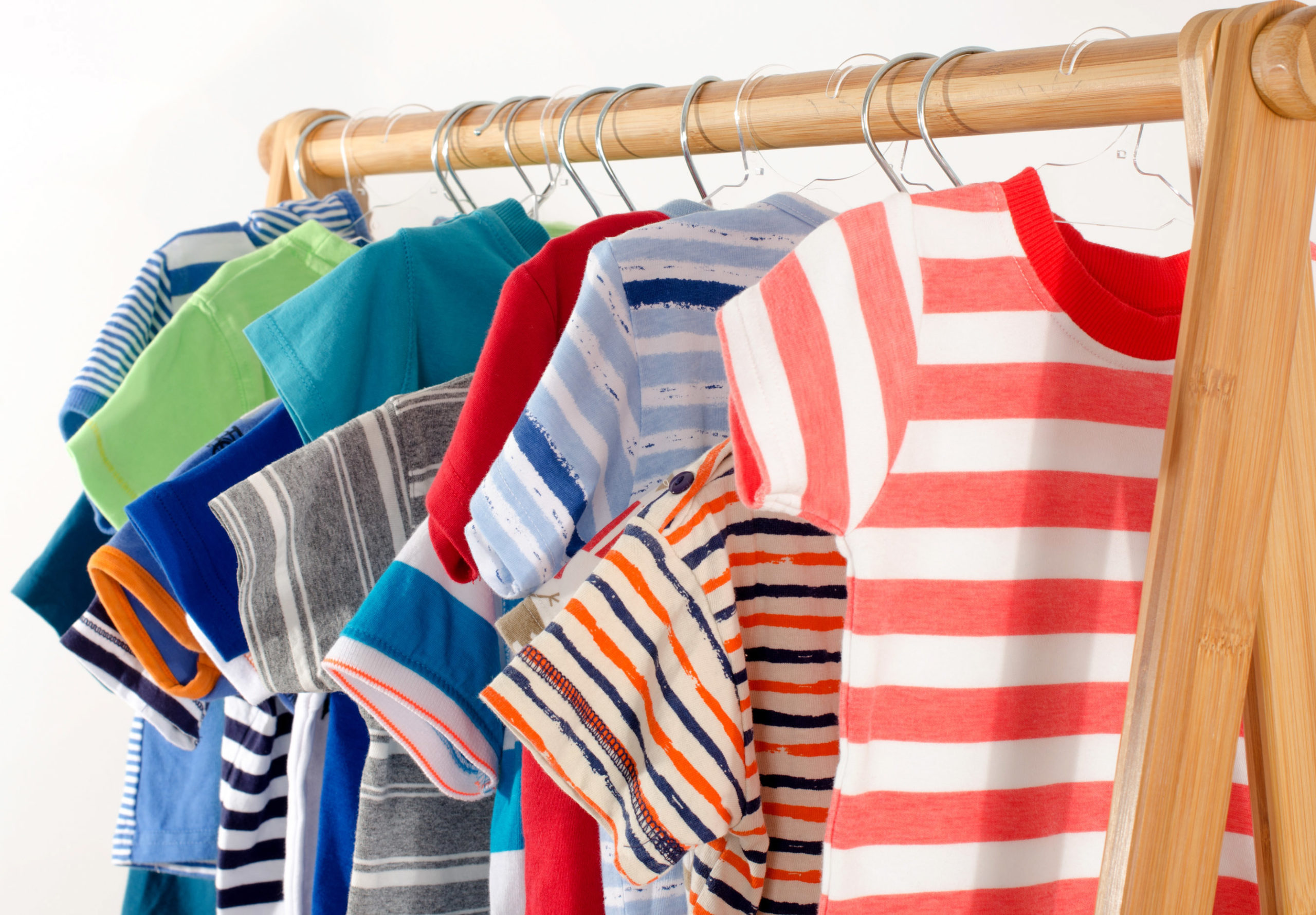 Dressing closet with clothes arranged on hangers.Colorful wardrobe of newborn,kids, toddlers, babies full of all clothes.Many t-shirts,pants, shirts,blouses, onesie hanging