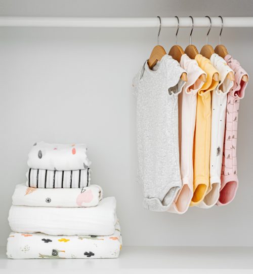 Set of baby bodysuits for a newborn girl and boy on hangers in white wardrobe. Motherhood, cleaning home kids wardrobe. Minimal fashion concept.